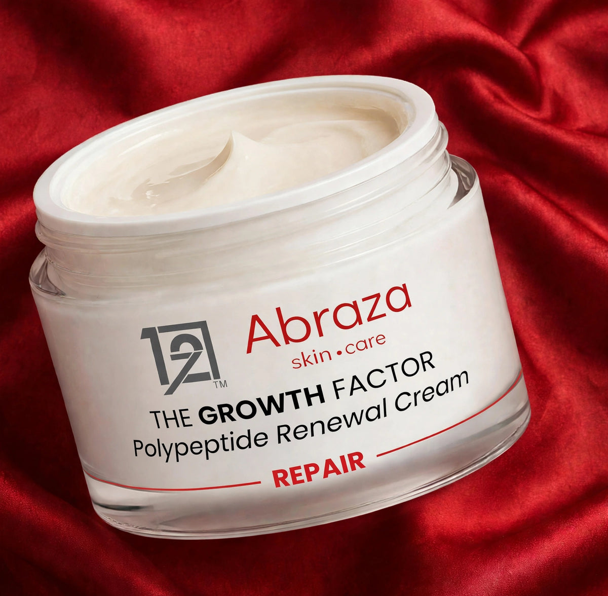 Open jar of Abraza The Growth Factor Polypeptide Renewal Cream on red silk, cream swatched on a hand
