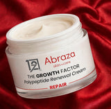 Open jar of Abraza The Growth Factor Polypeptide Renewal Cream on red silk, cream swatched on a hand